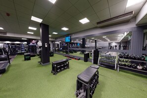 A gym with various exercise equipment, a treadmill, weights, and a mirror wall.