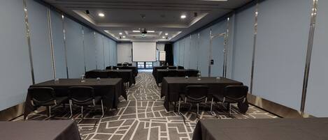 A conference room with tables and chairs, a projector screen, and a patterned carpet.