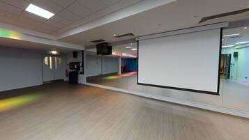 A spacious room with a large whiteboard, wooden flooring, and a view of a colorful corridor.