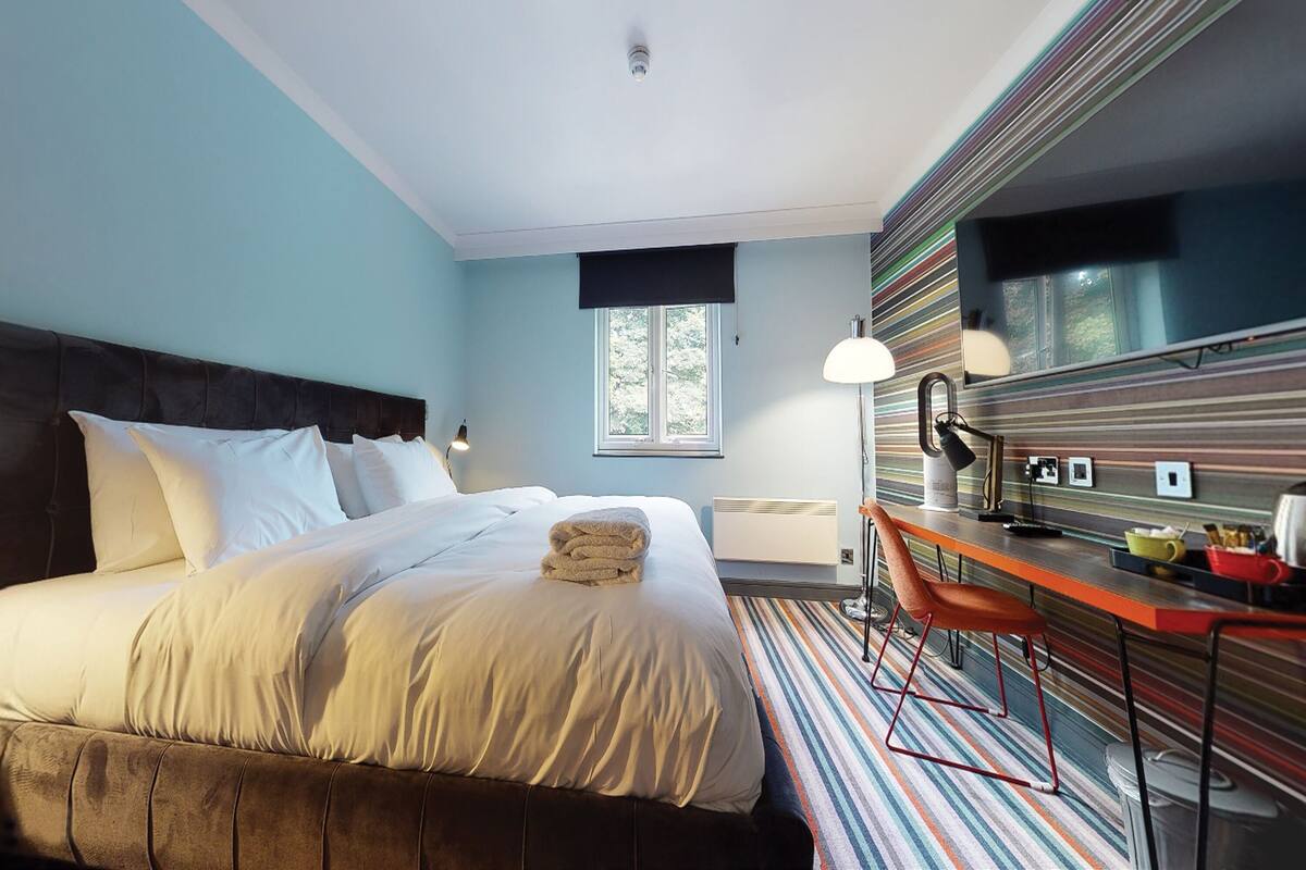 A modern hotel room with a large bed, a desk, and a striped wall.