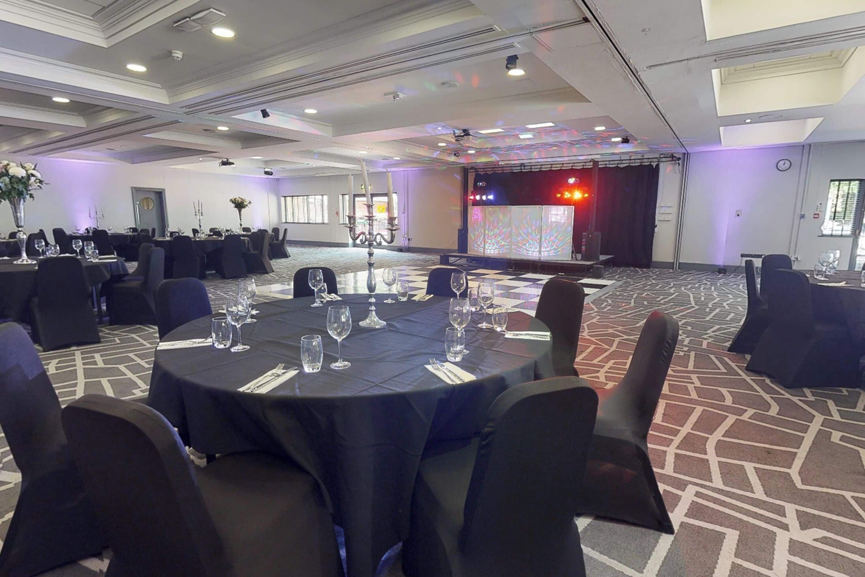 A conference room with round tables, black tablecloths, and chairs.