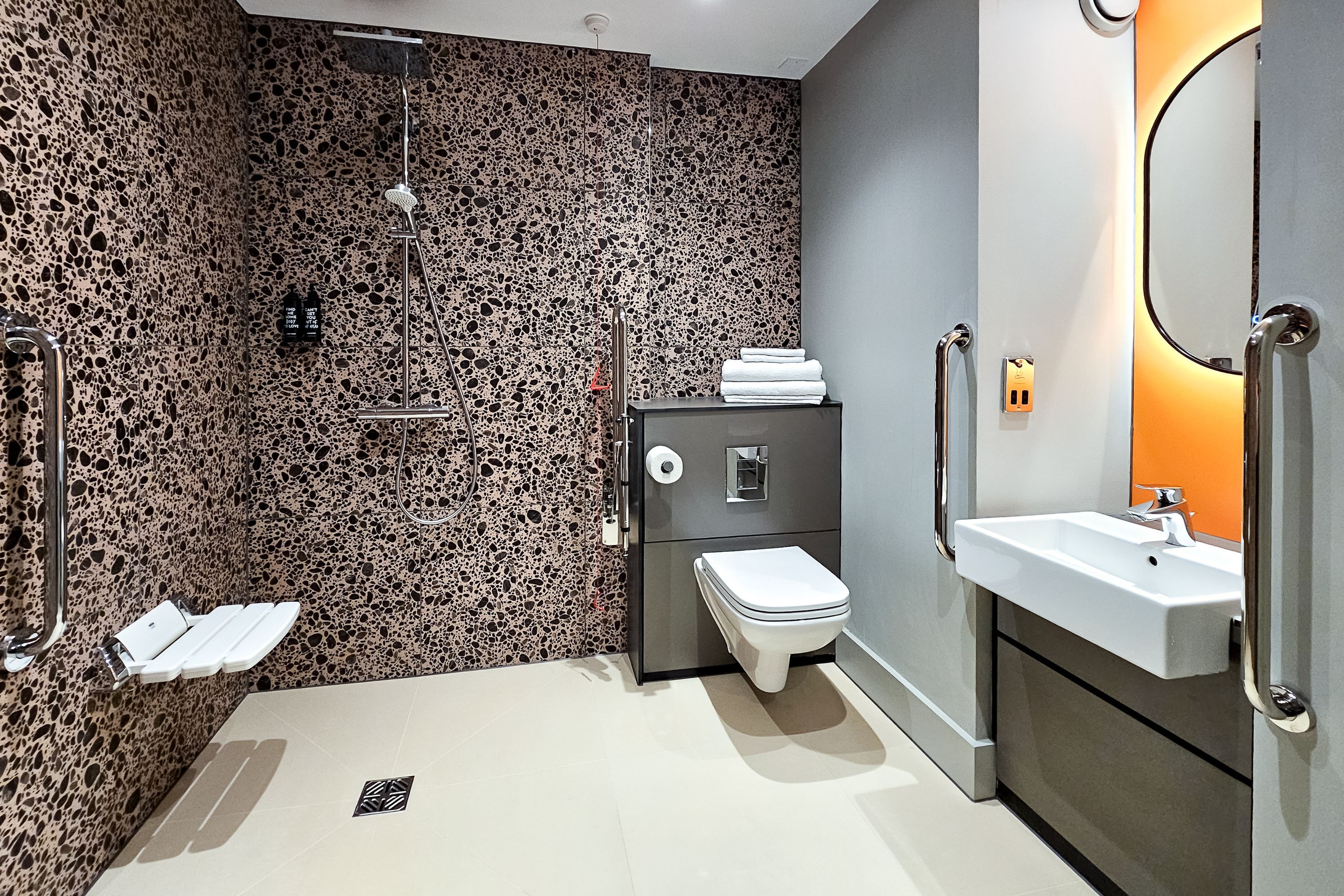 A modern bathroom with a granite backsplash, a toilet, a sink, and a shower.
