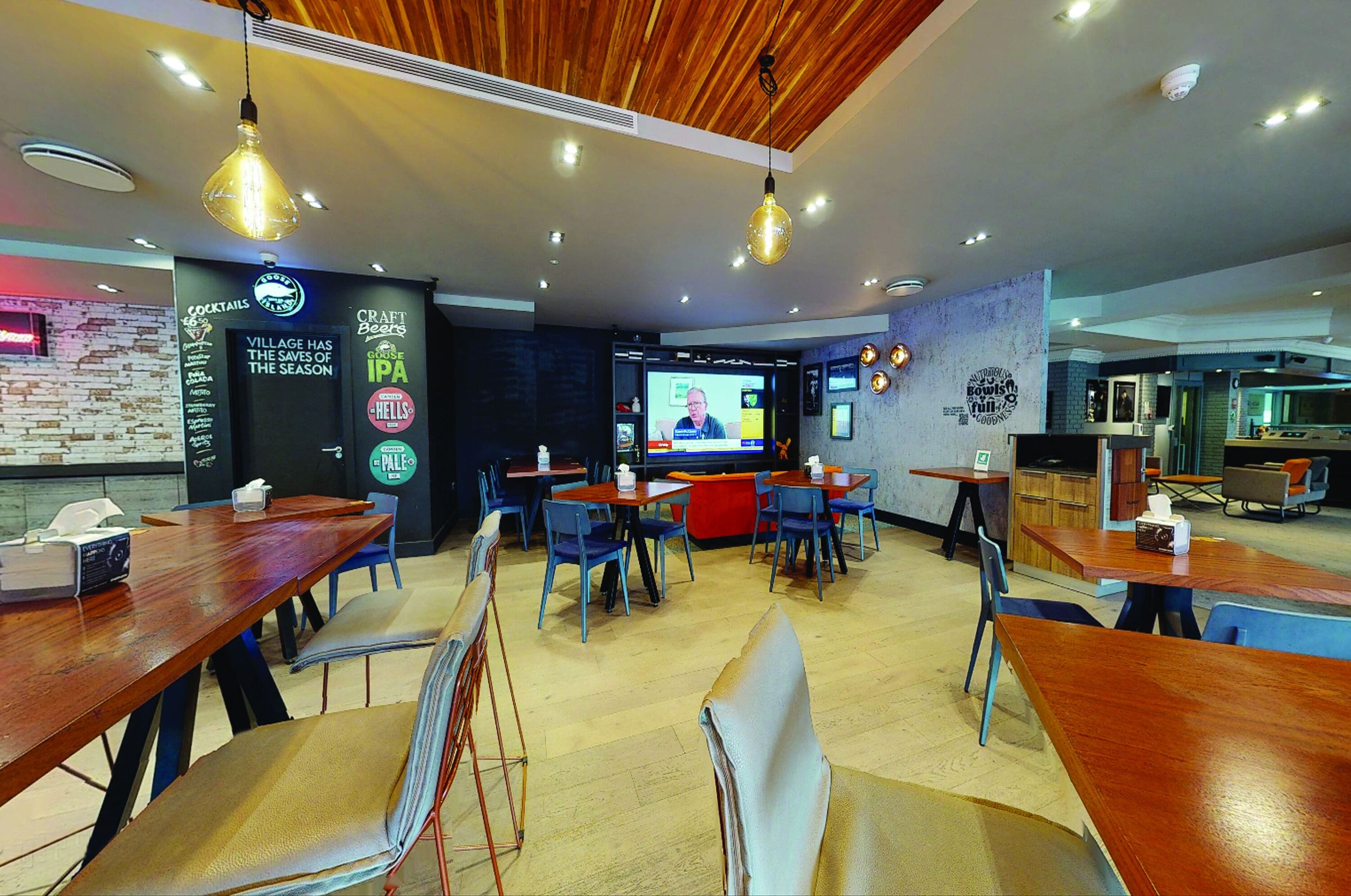 Un restaurant avec des tables et des chaises en bois, un écran de télévision et un tableau affichant le menu.