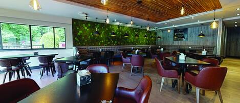 A modern restaurant with wooden ceiling, green wall, and red chairs. Tables are arranged for dining.