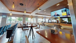 A spacious restaurant with wooden ceiling and modern lighting, a bar area with a large screen displaying a sports event, and outdoor seating by large windows. - Village Hotel Leeds North (Leeds)