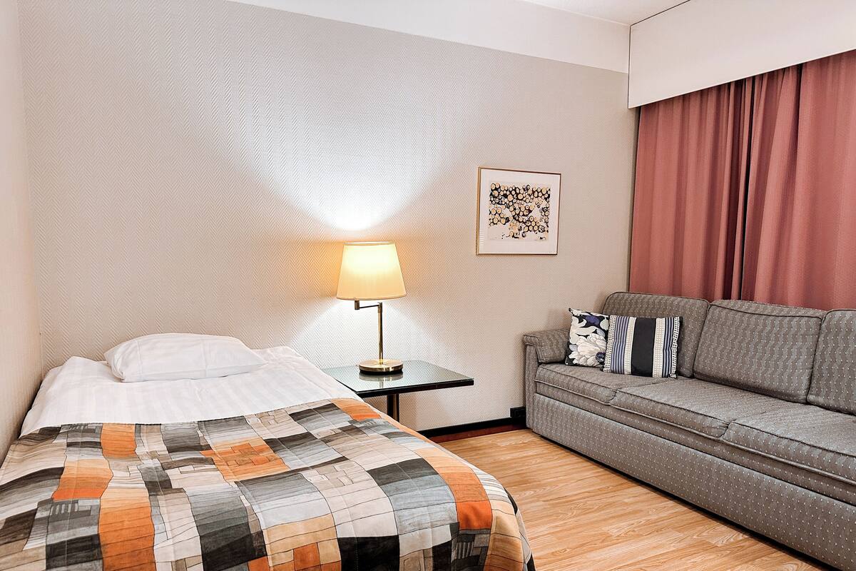 A hotel room with a bed, a sofa, a lamp, and a framed picture on the wall.