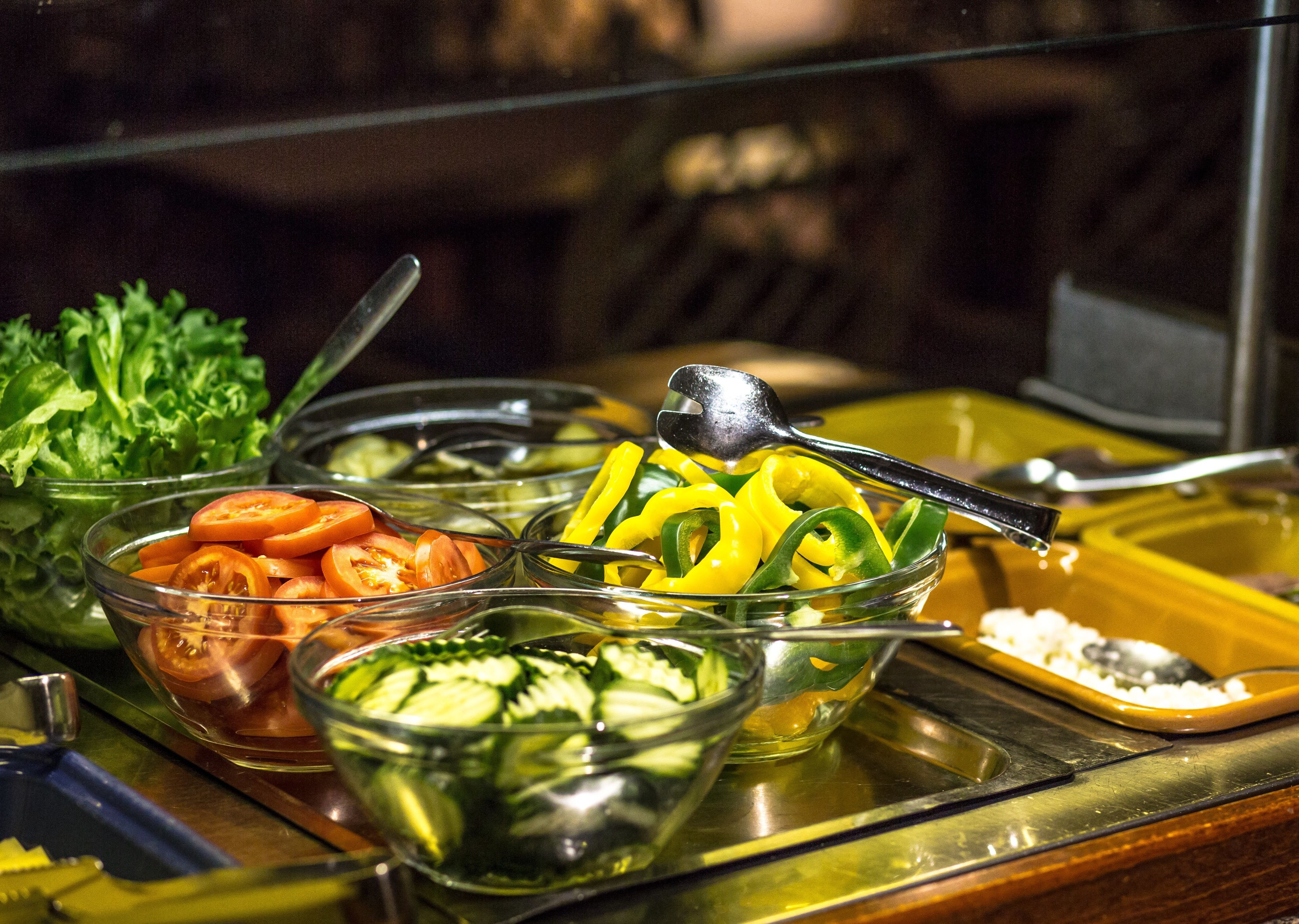 A buffet with various food items including sliced tomatoes, cucumbers, and yellow bell peppers.