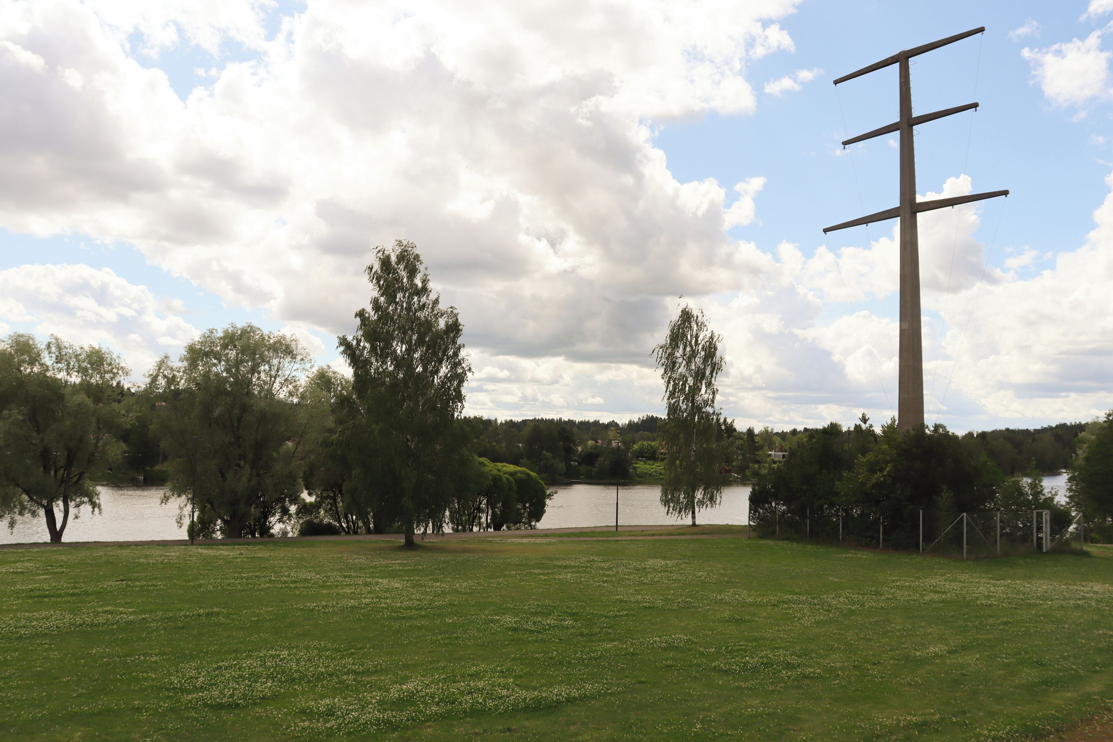 Un champ herbeux avec une grande croix, des arbres et une étendue d’eau.