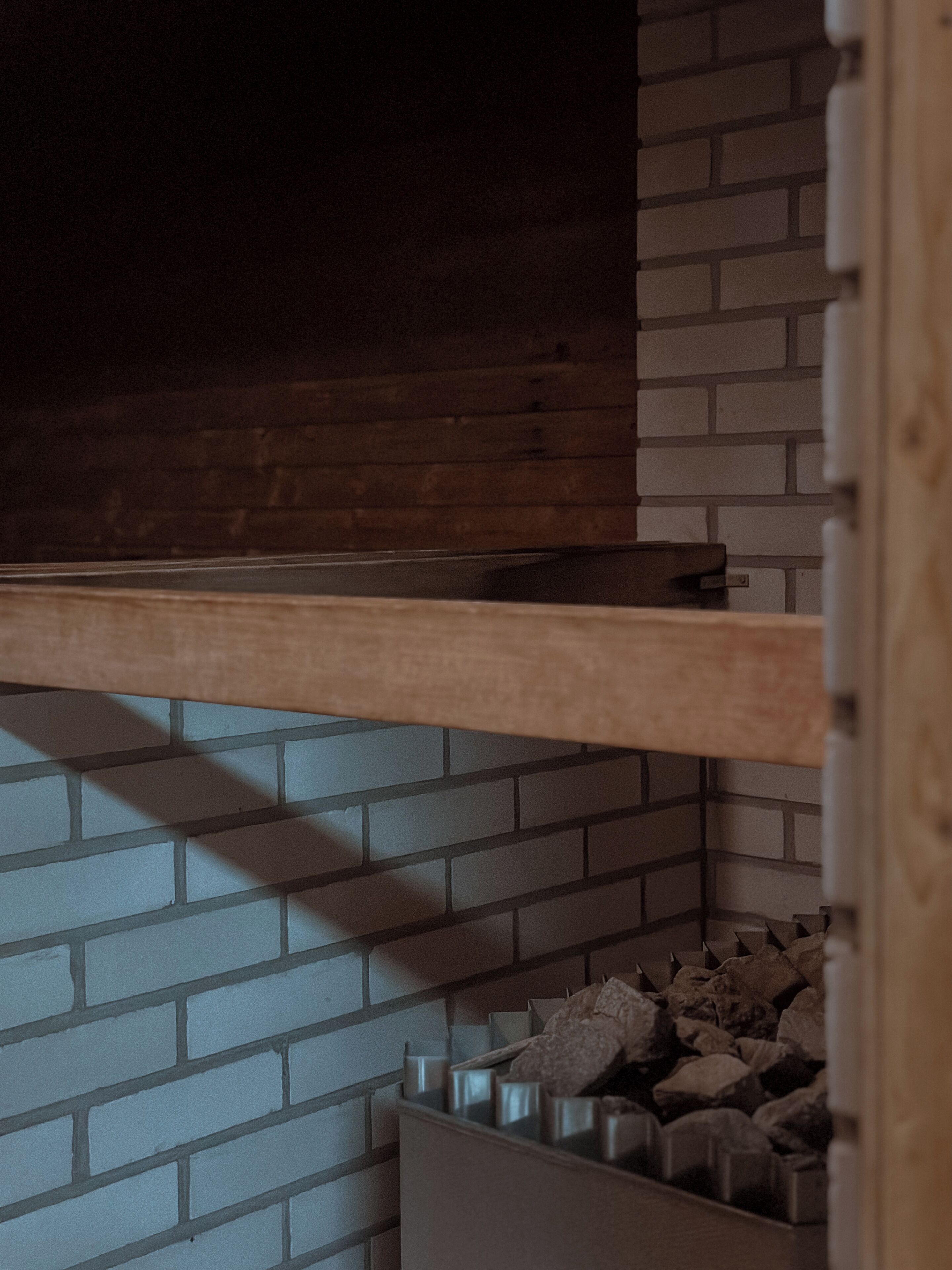 Una habitación con pared de ladrillo, un estante de madera y un mueble de almacenamiento con contenedores metálicos.