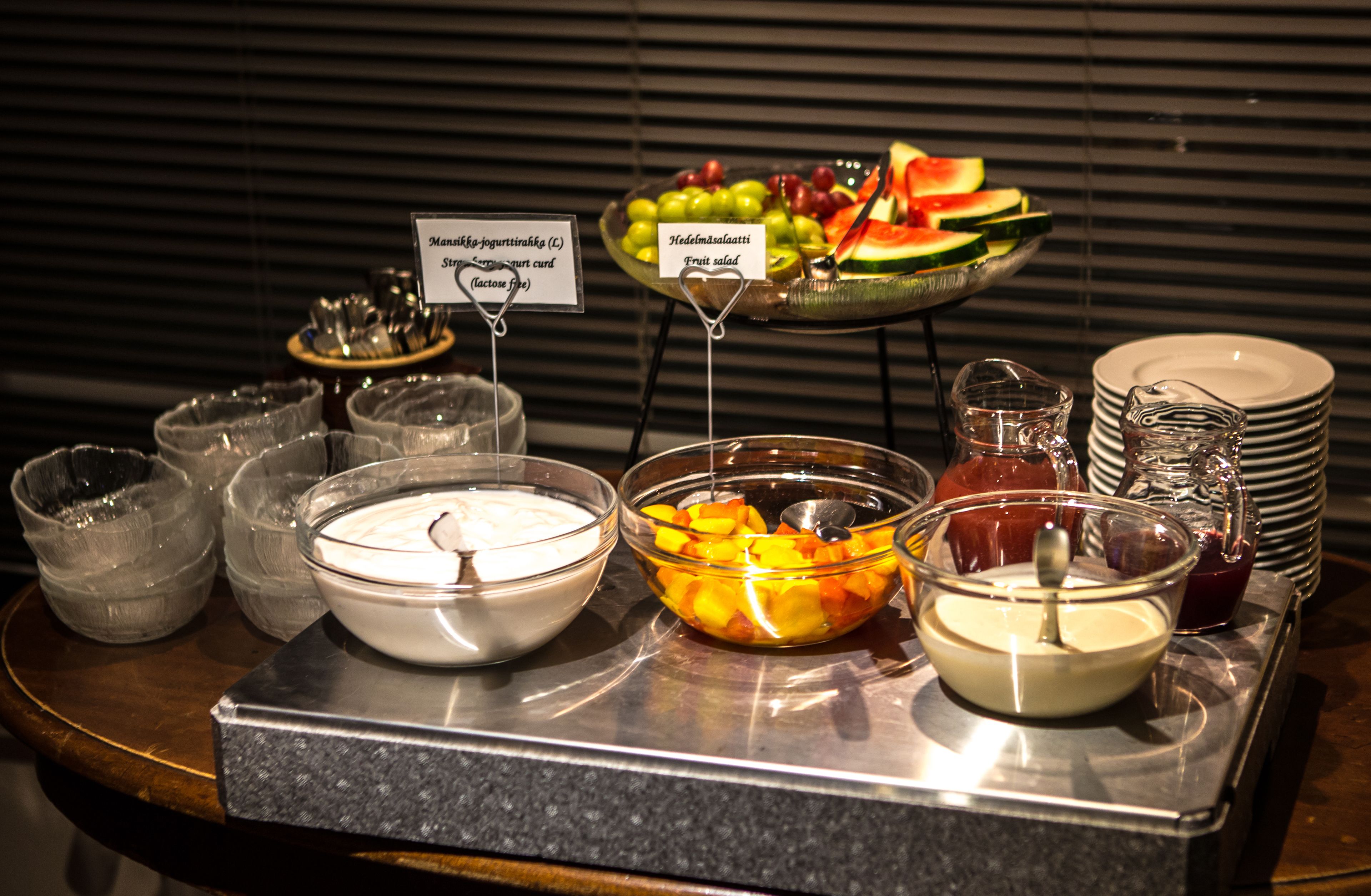 A buffet with various food items including yogurt, fruit salad, and a bowl of mangoes.