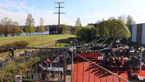 An outdoor seating area with tables and chairs, a pathway, and a view of a lake and trees. - Hotel Sommelo (Kouvola)