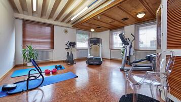Een ruime kamer met een loopband, een hometrainer en gewichten.