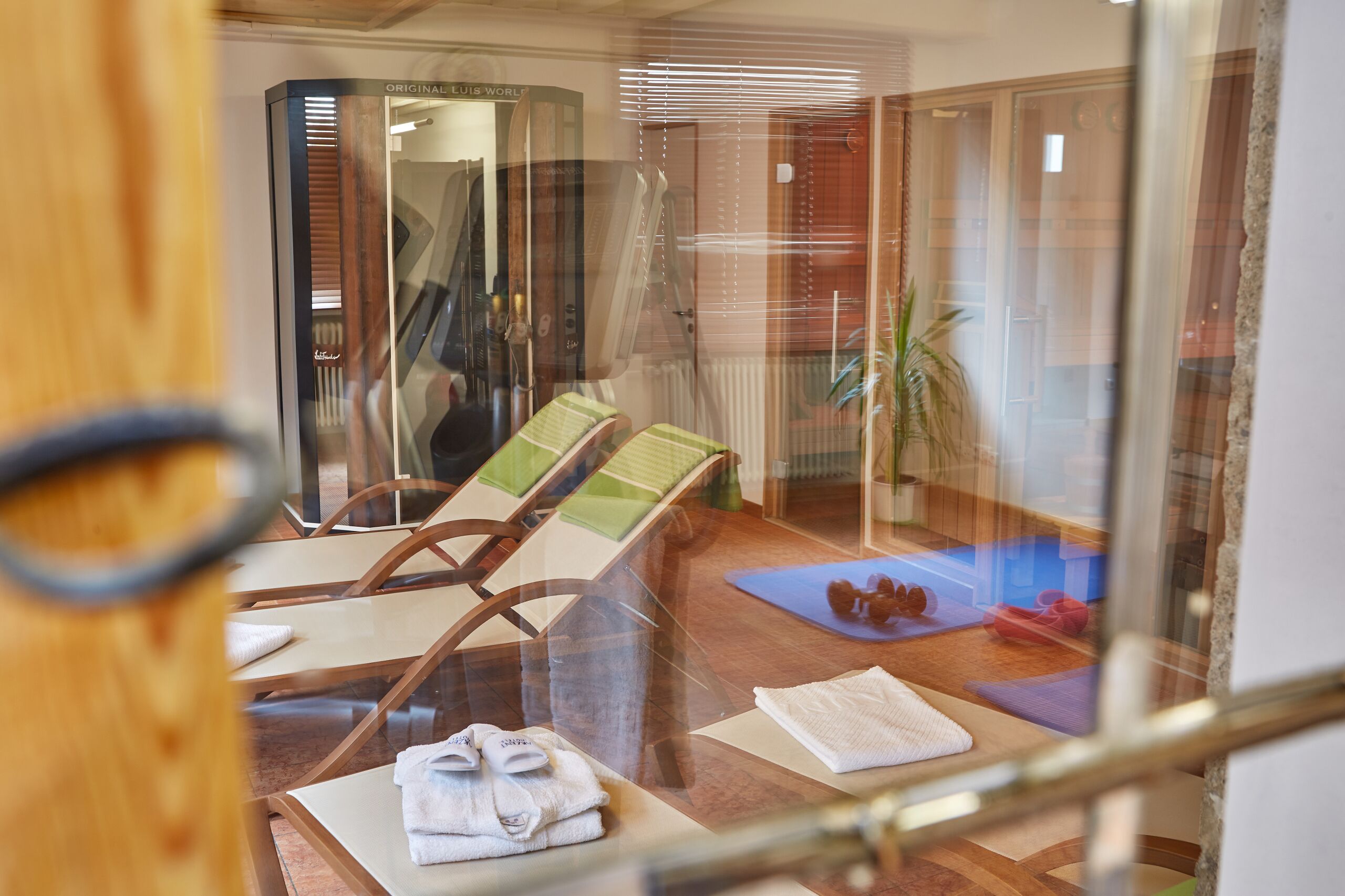 Una habitación con separador de vidrio, muebles de madera, una camilla de masaje y una esterilla para ejercicios.