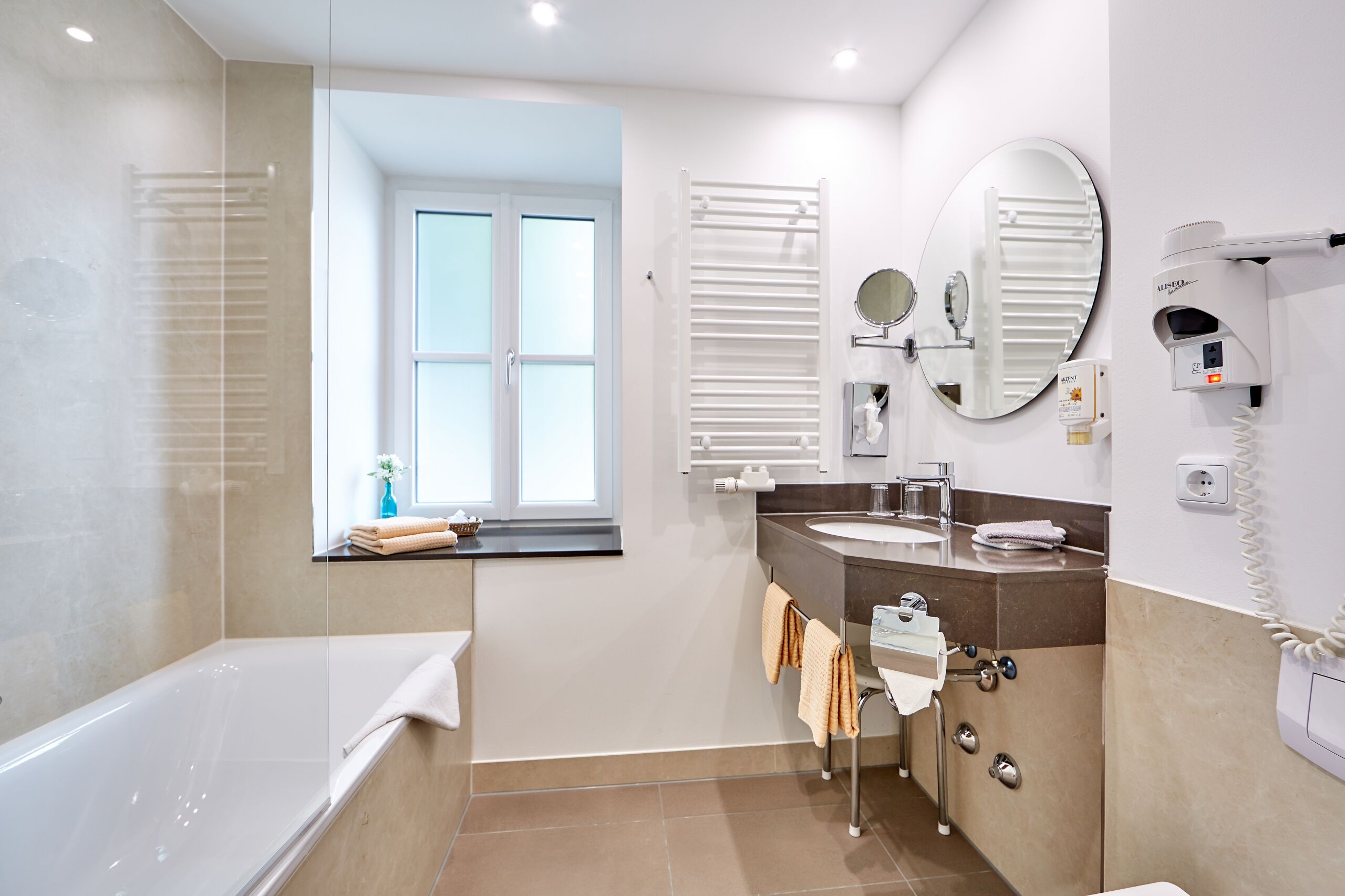 A modern bathroom with a bathtub, a sink, a mirror, and a hairdryer.