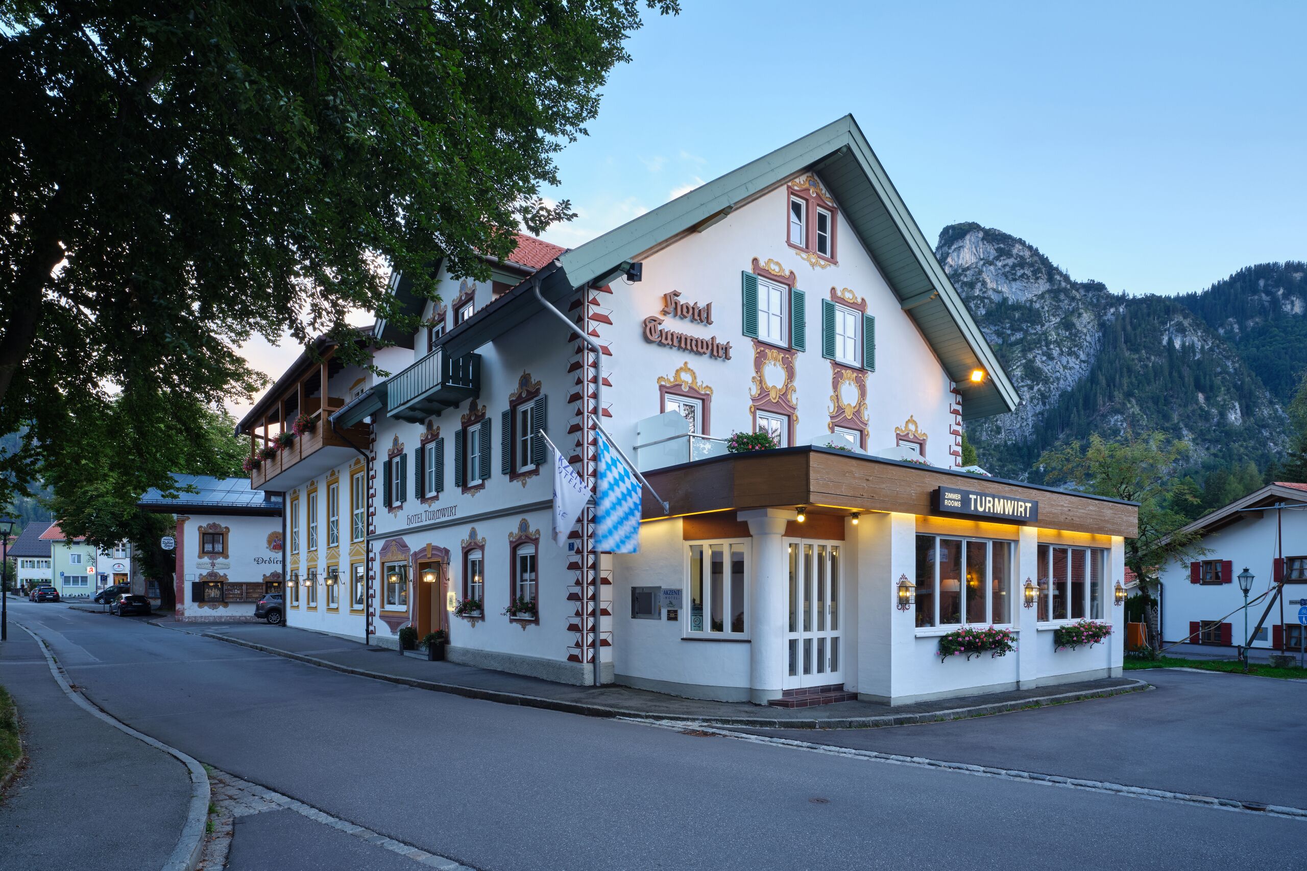 A traditional European hotel with a prominent sign, a balcony, and a mountain backdrop.