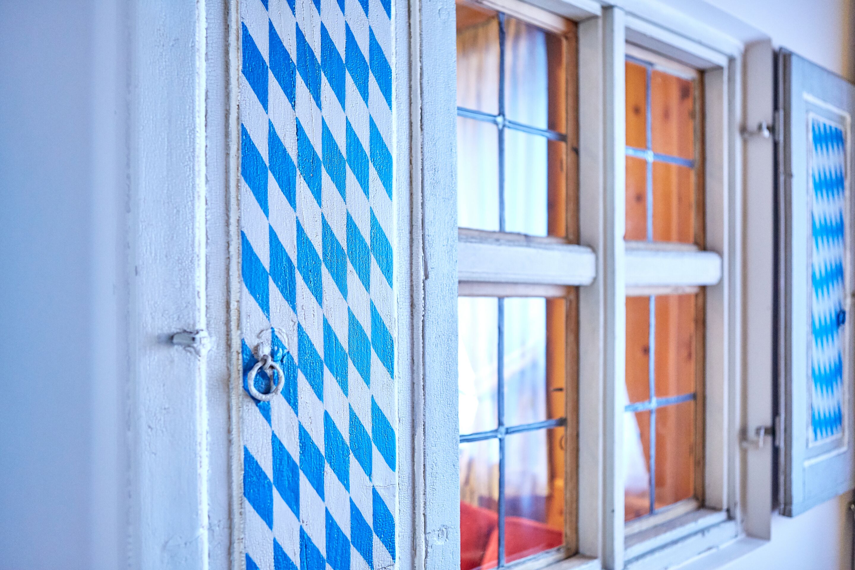 Una ventana con un estampado azul y blanco a cuadros, contraventanas de madera y un tirador de metal en forma de anillo.