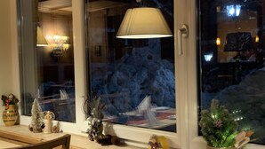 Una habitación con un ventanal grande, un banco de madera y diversas decoraciones, incluyendo un pequeño árbol de Navidad y una figurita.