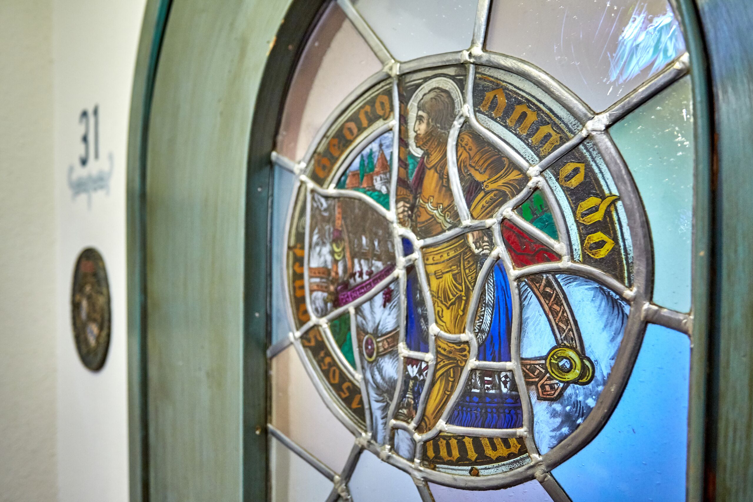 A stained glass window with a figure and text, part of a building's interior.