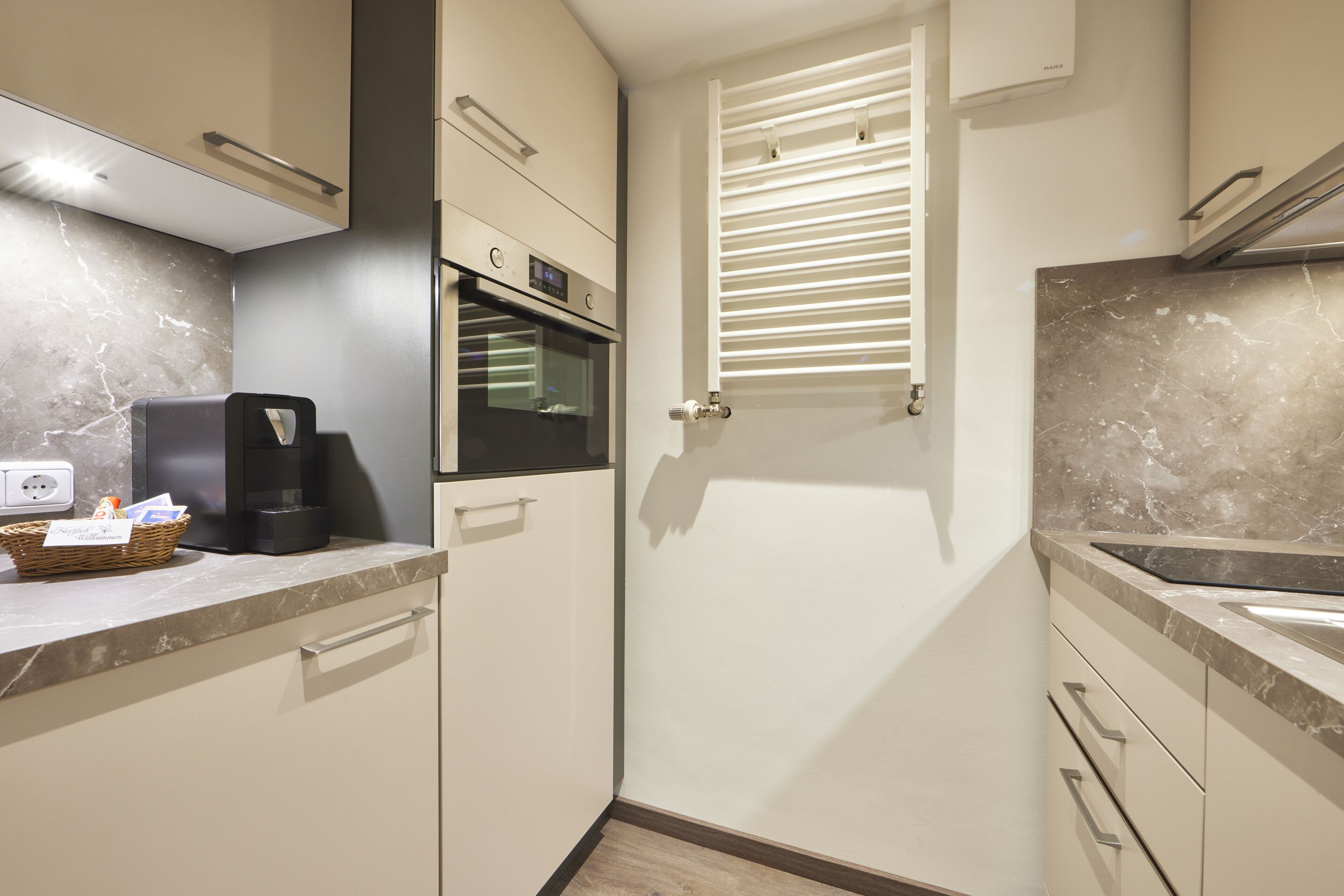 A modern kitchen with a built-in oven, a coffee machine, and a basket of items on the counter.