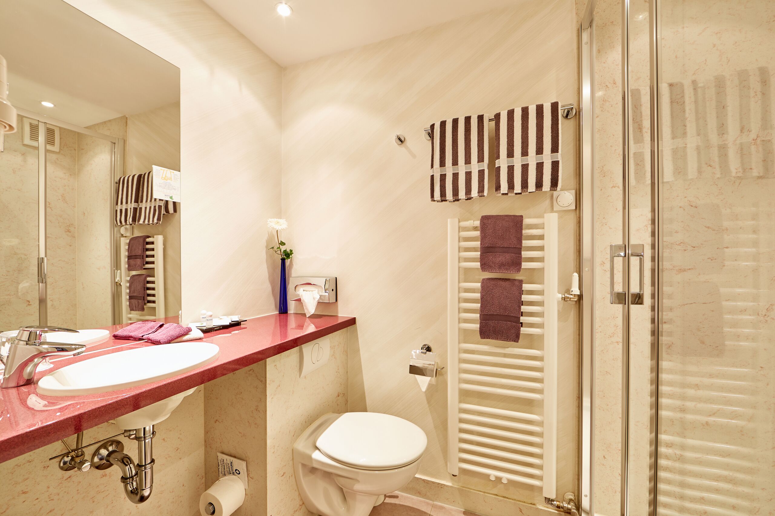 A modern bathroom with a marble sink, a toilet, a glass shower enclosure, and a towel rack with striped towels.