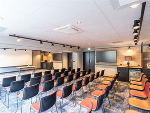 A conference room with rows of chairs, a projector screen, and a television on the wall. - Kyriad Paris Nord - Porte de Saint Ouen (Saint-Ouen)