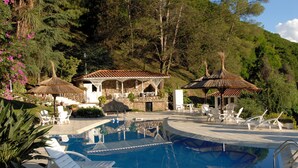 Un espace piscine avec des chaises longues, un bâtiment en pierre et un gazebo à toit de chaume.