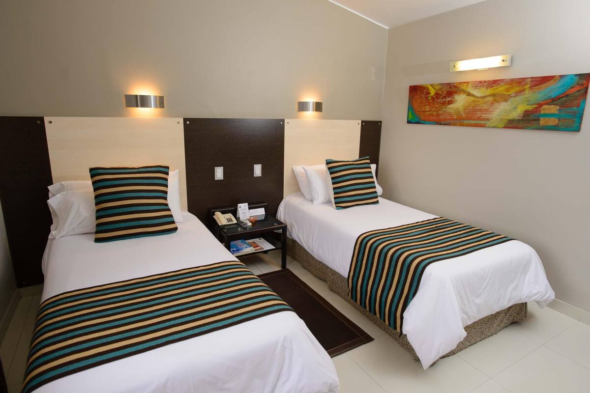 A hotel room with two beds, a nightstand, a telephone, and a painting on the wall.