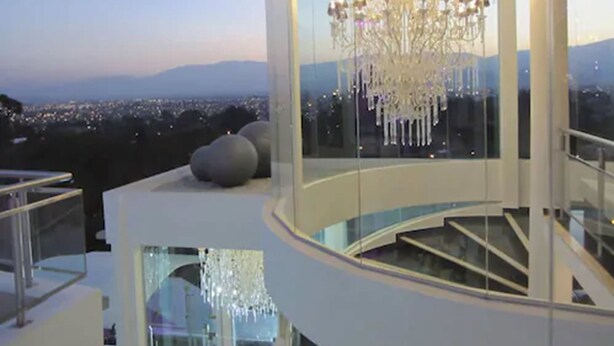 Un intérieur moderne agrémenté d’un grand lustre, d’une balustrade en verre et offrant une vue sur le paysage urbain.
