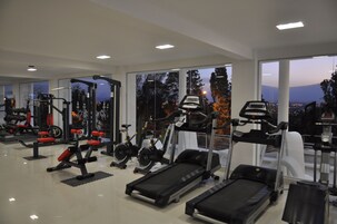 Un gimnasio con diverso equipo de ejercicio, amplias ventanas y vistas a un paisaje urbano al atardecer.