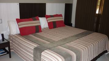 A neatly made bed with striped bedding and two pillows, a bedside table with a book, and a window with curtains.