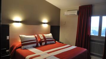 Ein Hotelzimmer mit einem Bett, zwei Wandleuchten, einer Klimaanlage und einem mit Vorhängen versehenen Fenster.