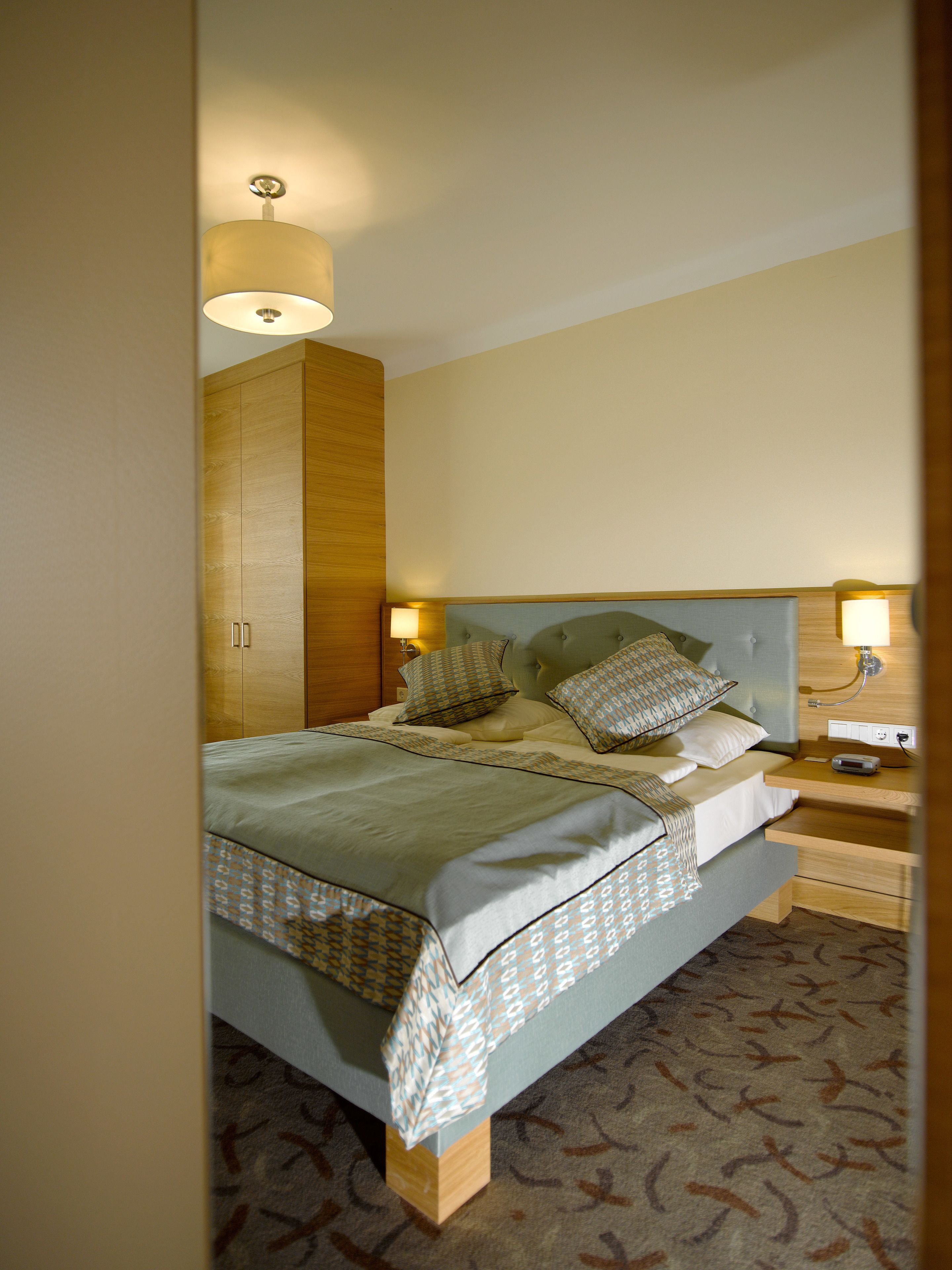 Una cama bien hecha con ropa de cama estampada, un armario de madera y lámparas de noche.