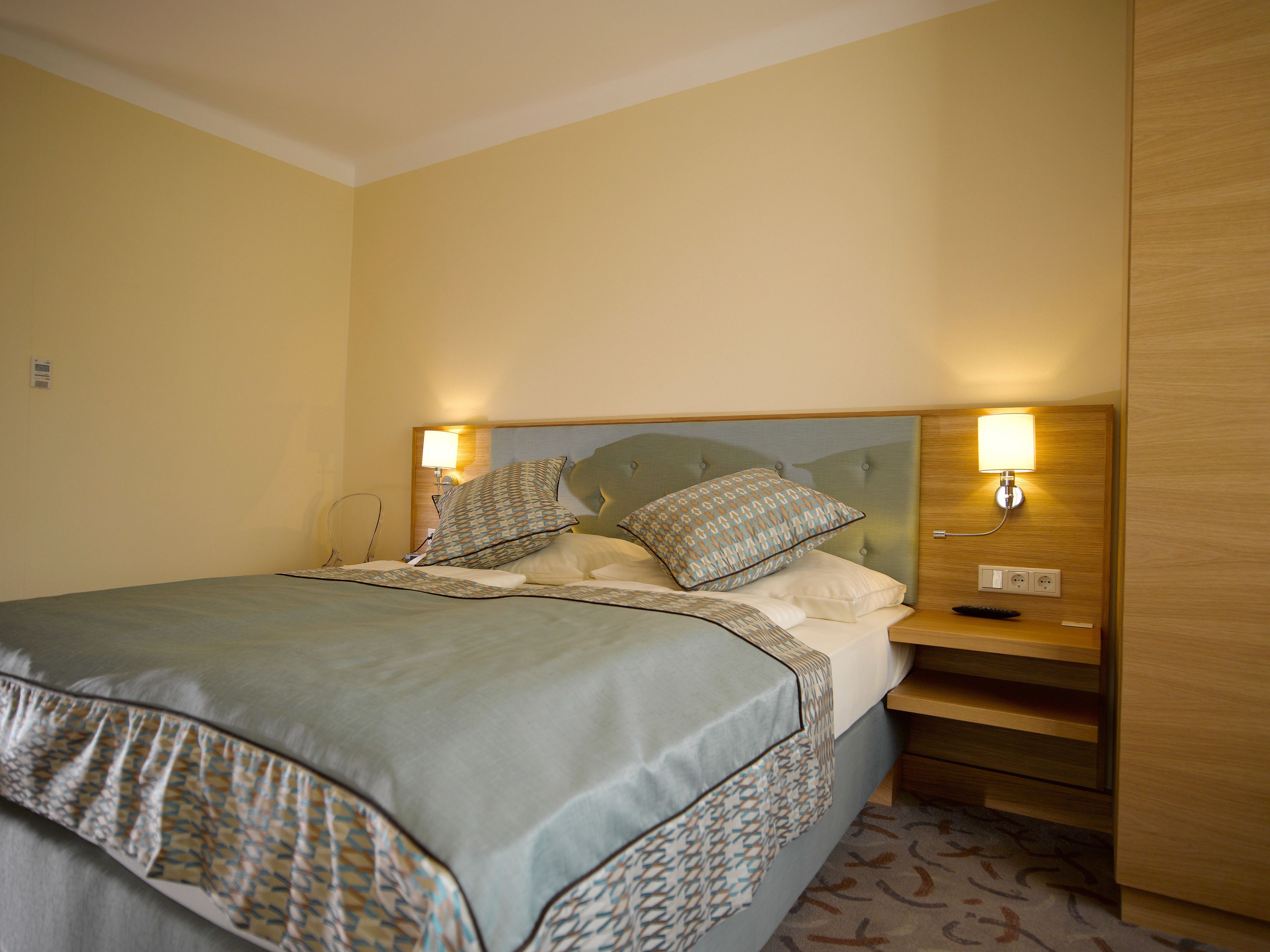 Una habitación de hotel con una cama, lámparas de noche y una mesita de noche de madera.