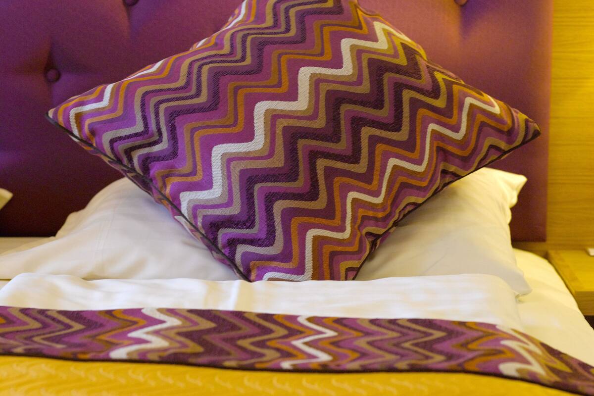 Una cama con un cojín estampado y una manta a rayas.