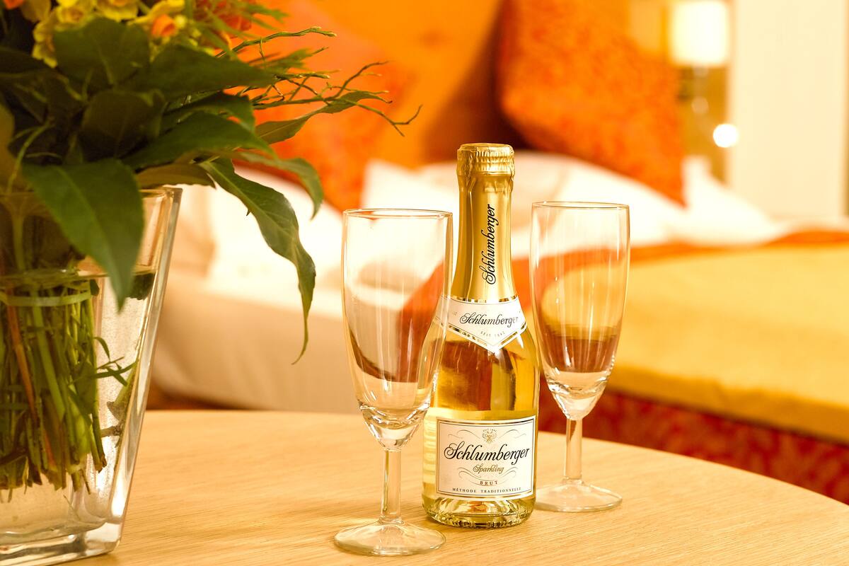 Una botella de vino espumoso Schlumberger, dos copas y un florero con flores sobre una mesa de madera.