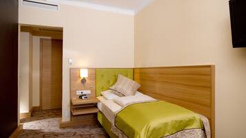A hotel room with a bed, bedside table, lamp, and a television on the wall.