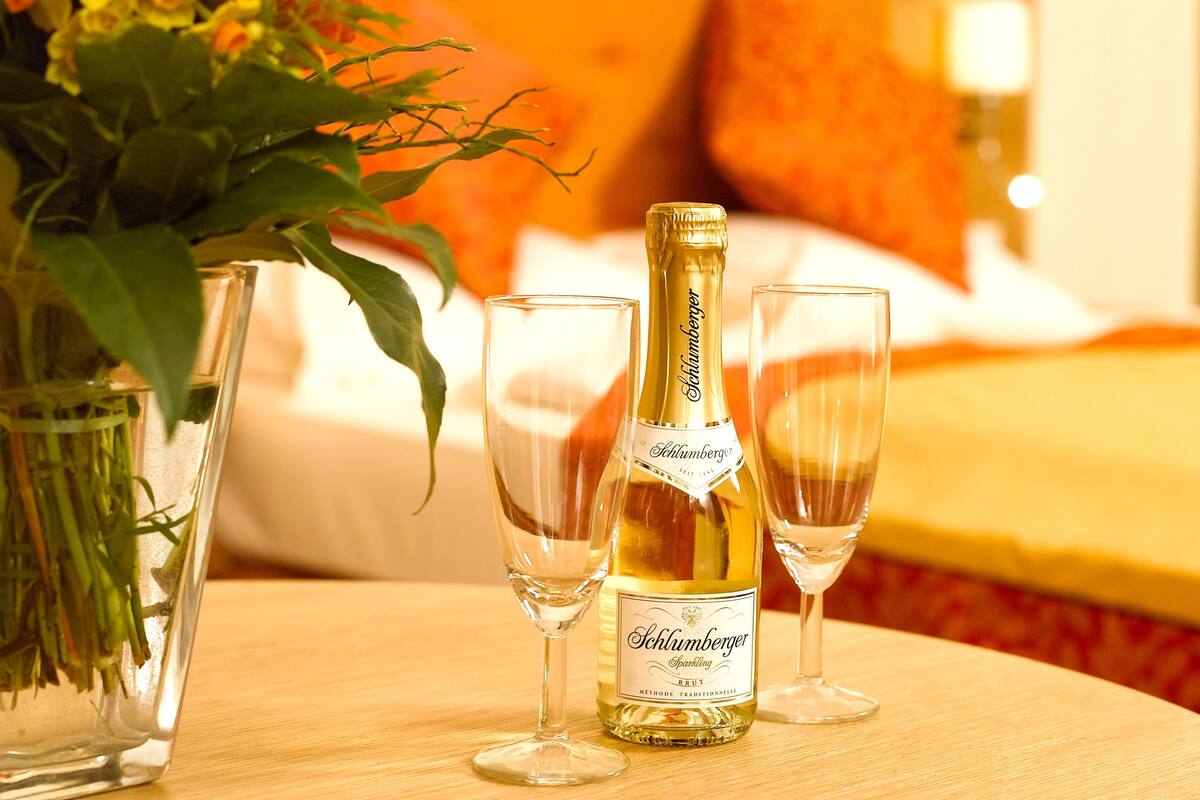 Una botella de vino espumoso Schlumberger, dos copas y un florero con flores sobre una mesa de madera.