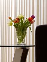 Un florero de vidrio transparente con tulipanes sobre una superficie reflectante.