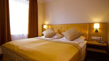 Habitación de hotel con una cama grande, dos lámparas de noche, una mesita de noche y una ventana con cortinas.