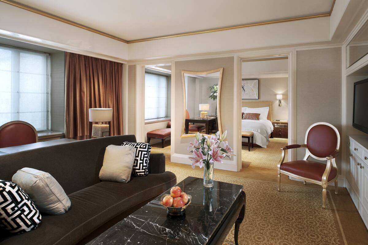 A hotel room with a dark brown sofa, a black marble coffee table, and a bed with white bedding.