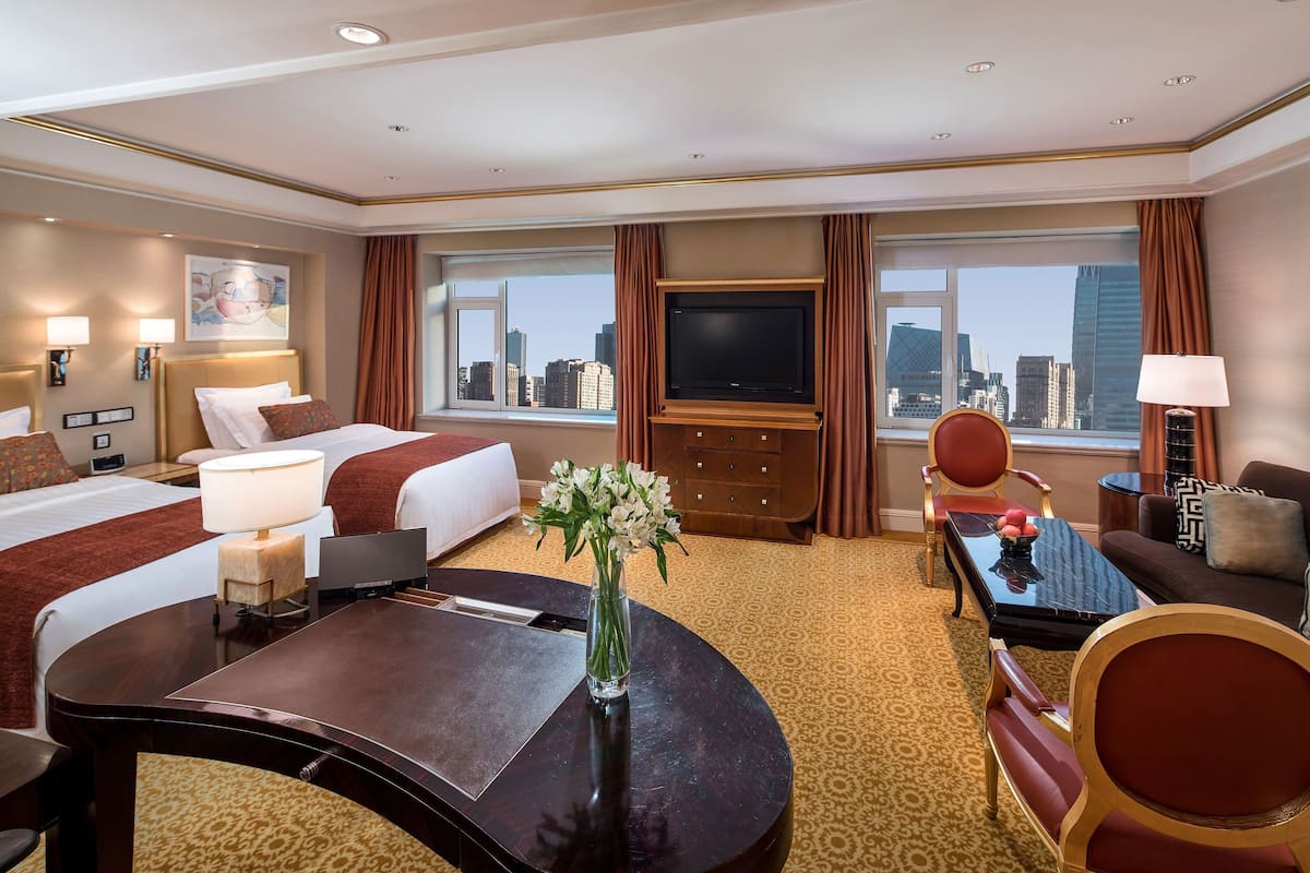 A hotel room with a bed, a desk, a chair, a TV, and a view of the city.