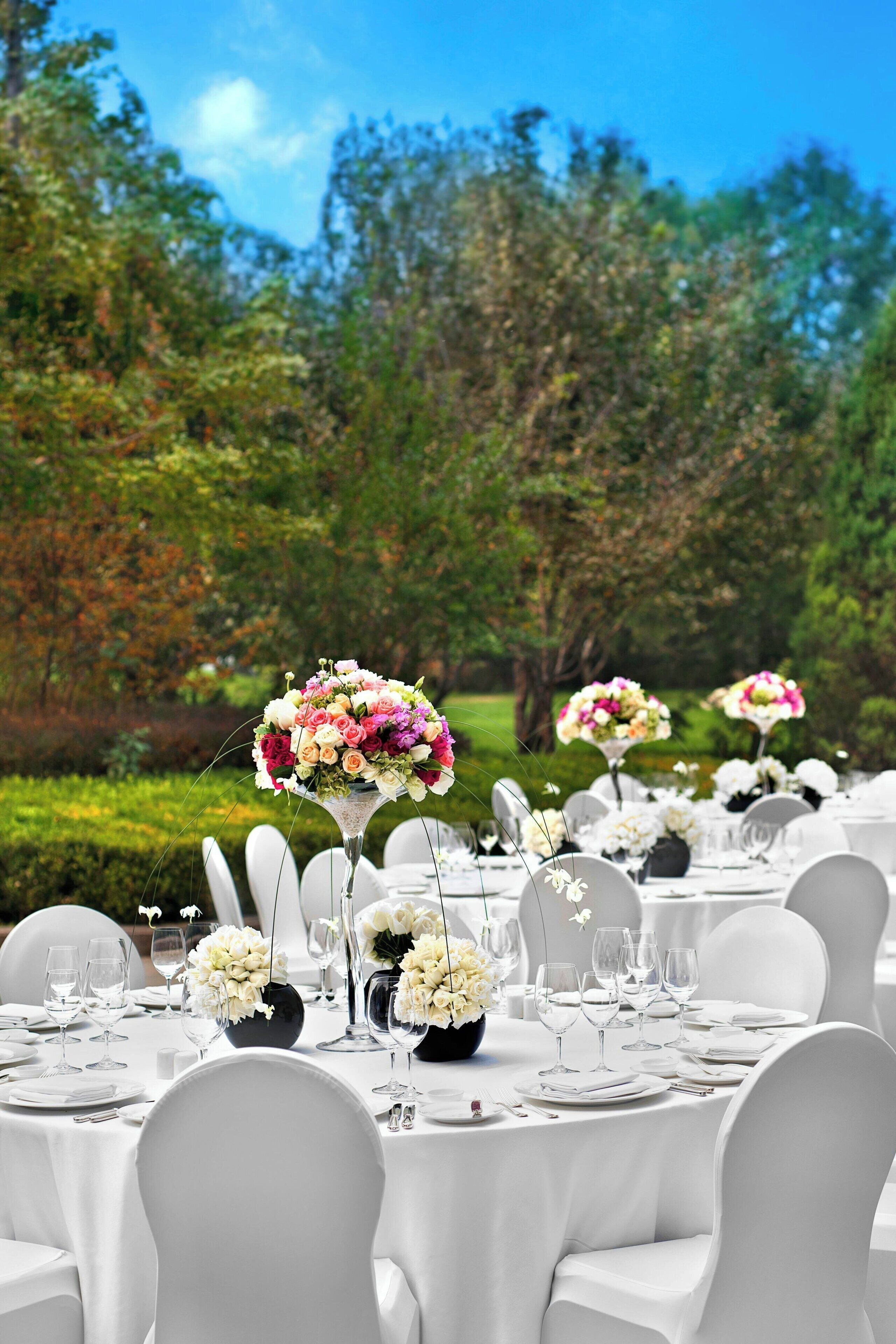 Un montaje formal para comidas al aire libre, con mesas redondas, sillas blancas y centros de mesa florales.