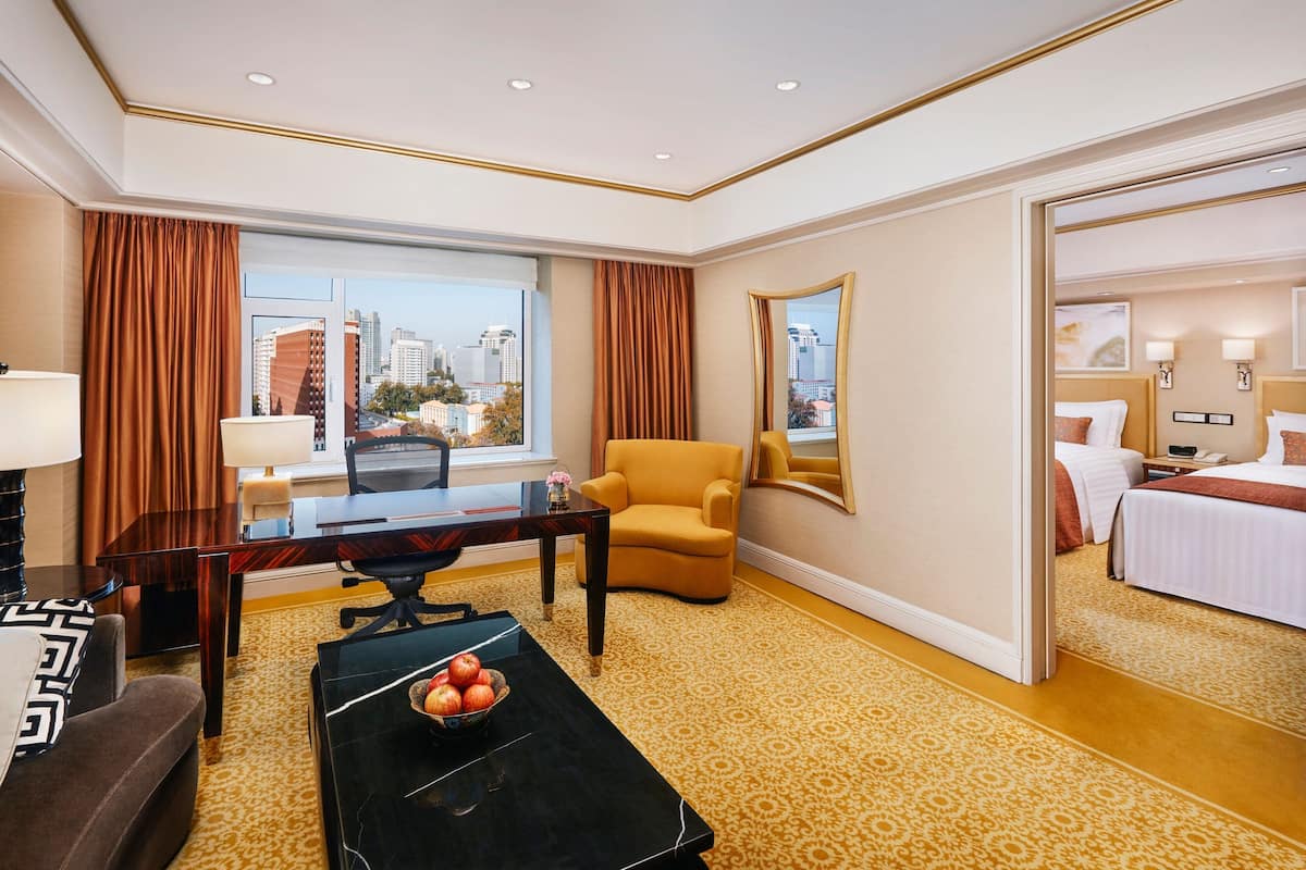 A hotel room with a large window, a desk, a comfortable armchair, a bed, and a mirror.
