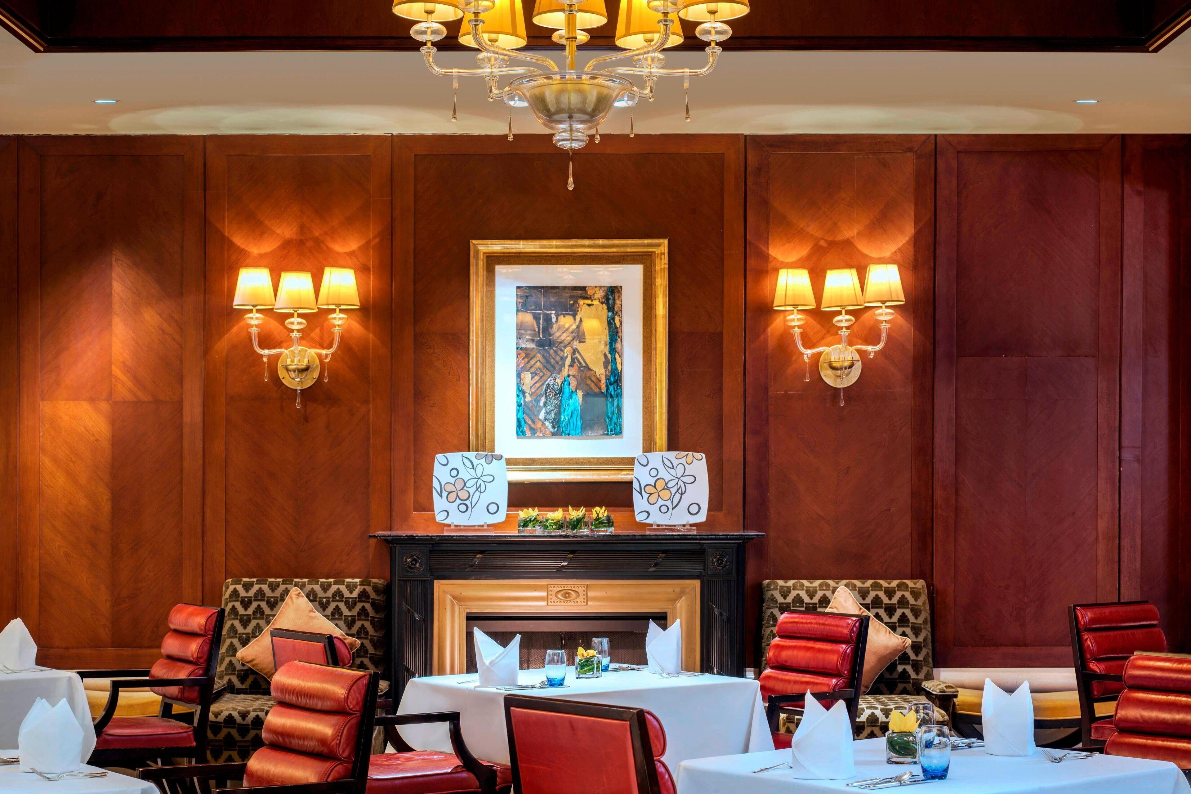 A dining area with a fireplace, red upholstered chairs, and a chandelier.