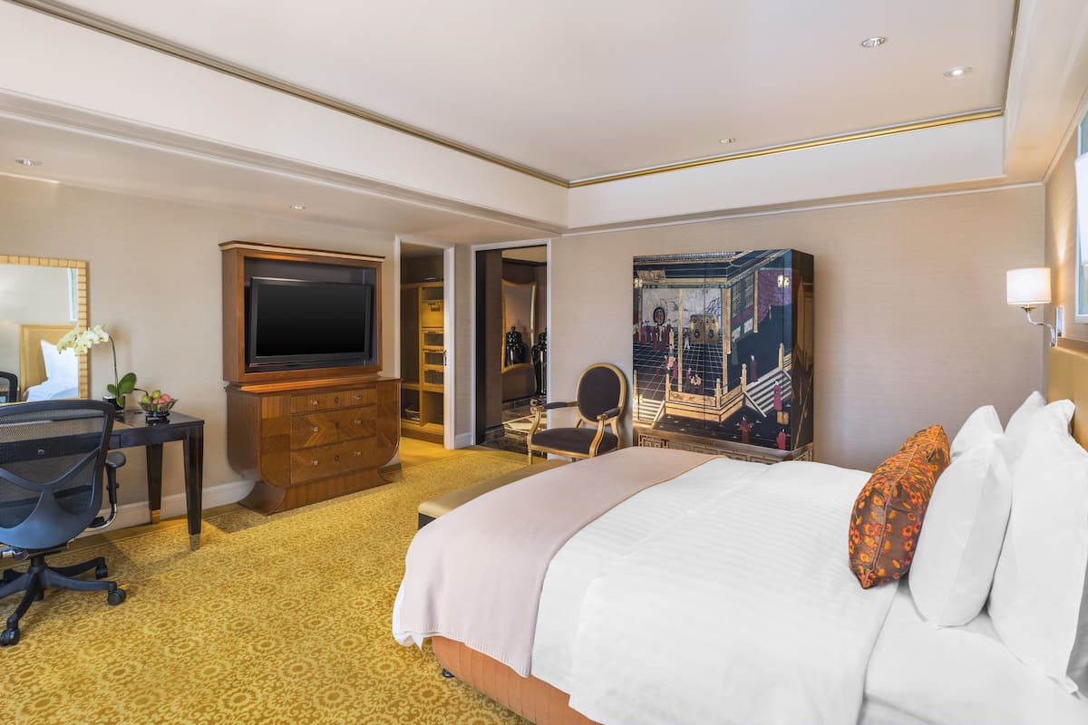 A hotel room with a large bed, a desk with a computer, a TV, a wardrobe, and a painting on the wall.