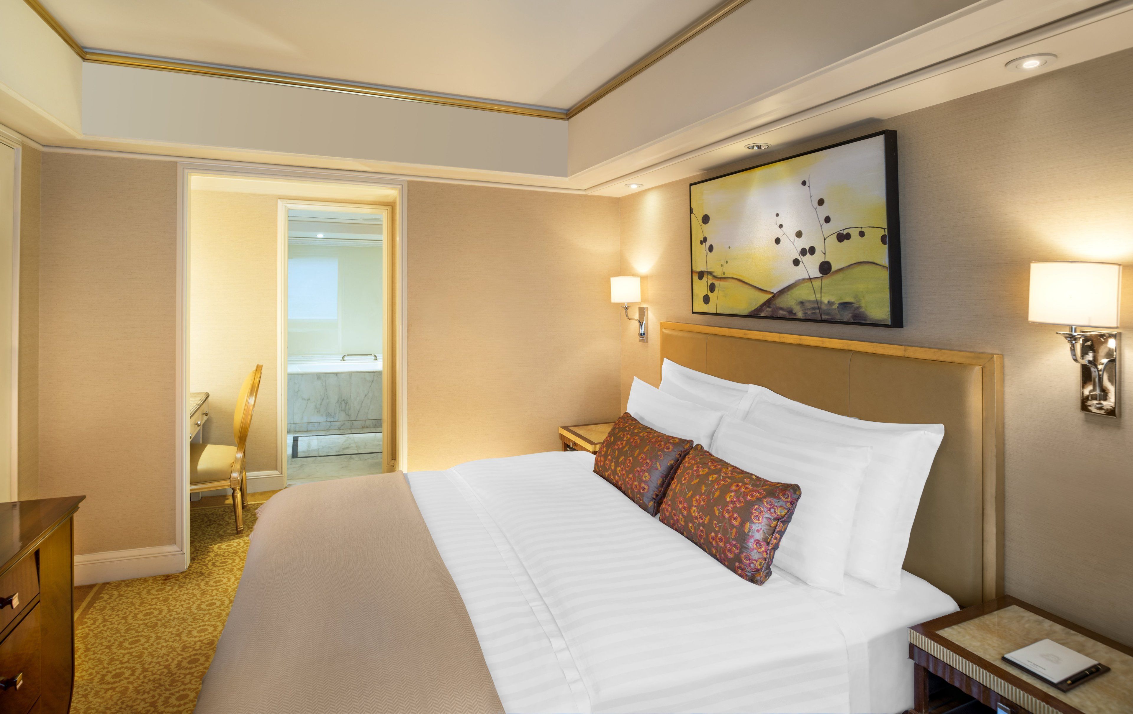 Une chambre d’hôtel avec un grand lit, une table de chevet, une lampe, un tableau au mur et une salle de bain visible à travers une porte ouverte.