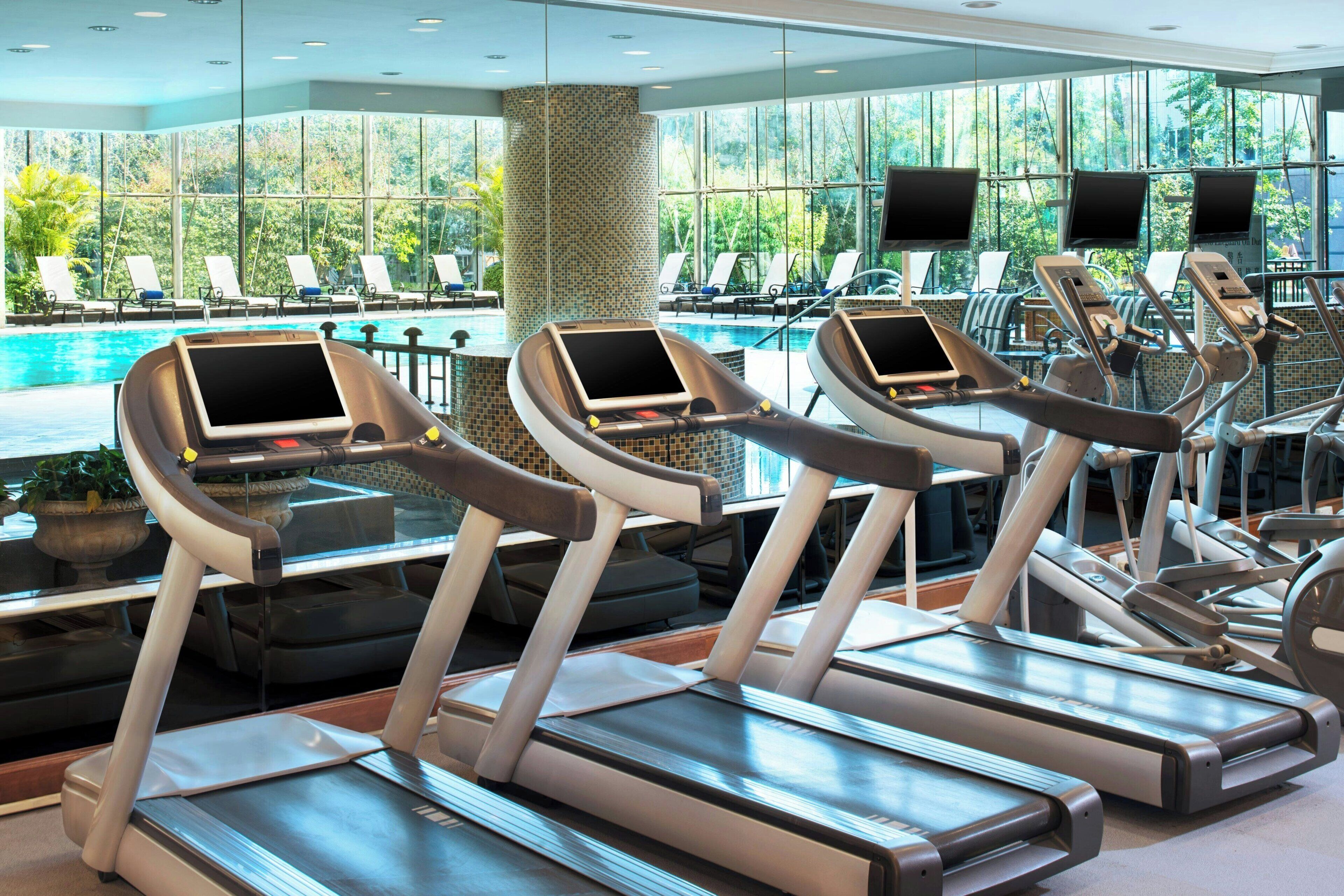 Een fitnessruimte met loopbanden, trainingsfietsen en een zwembadgedeelte met ligbedden.