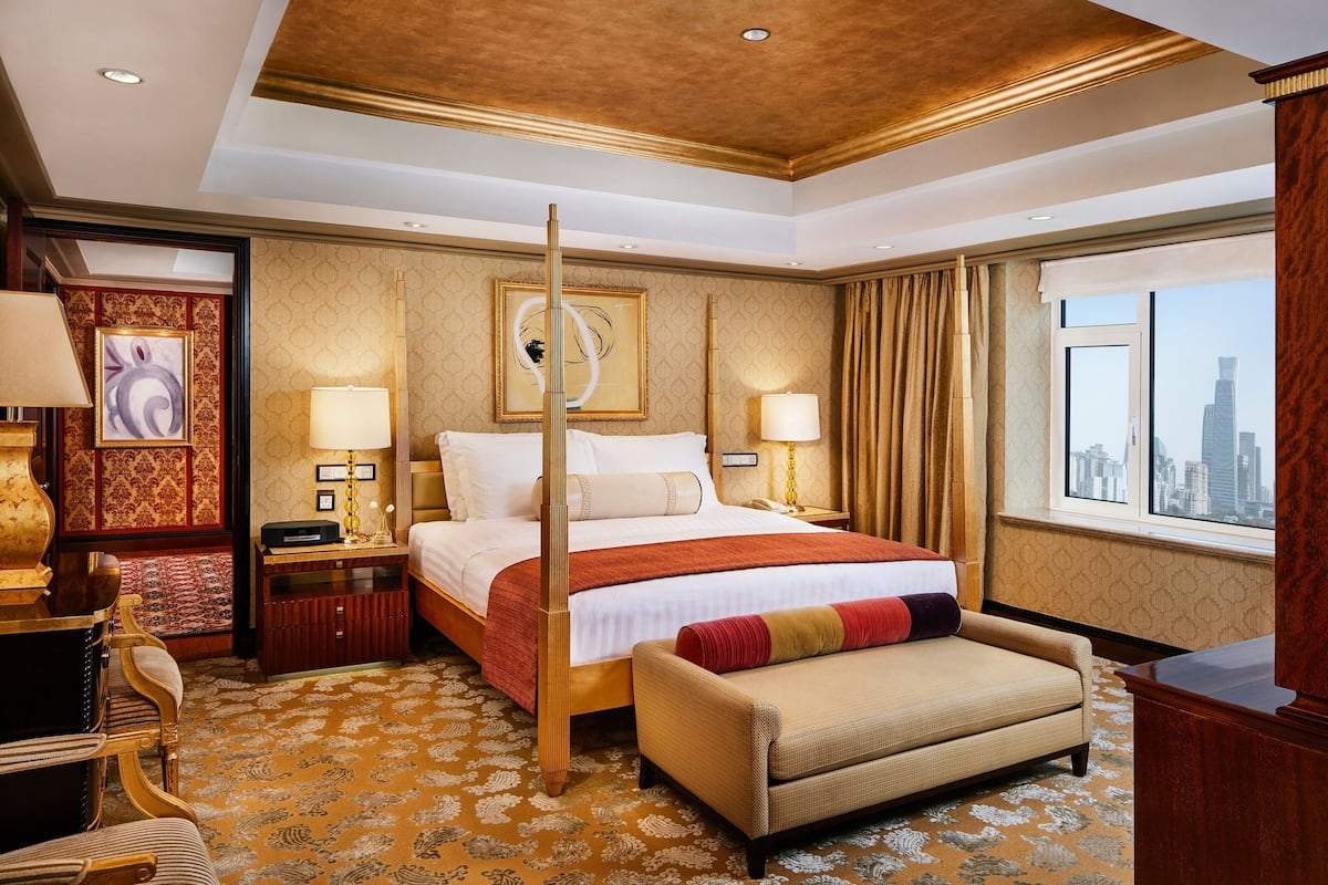 A hotel room with a large bed, a desk, a chair, a sofa, and a view of the city.