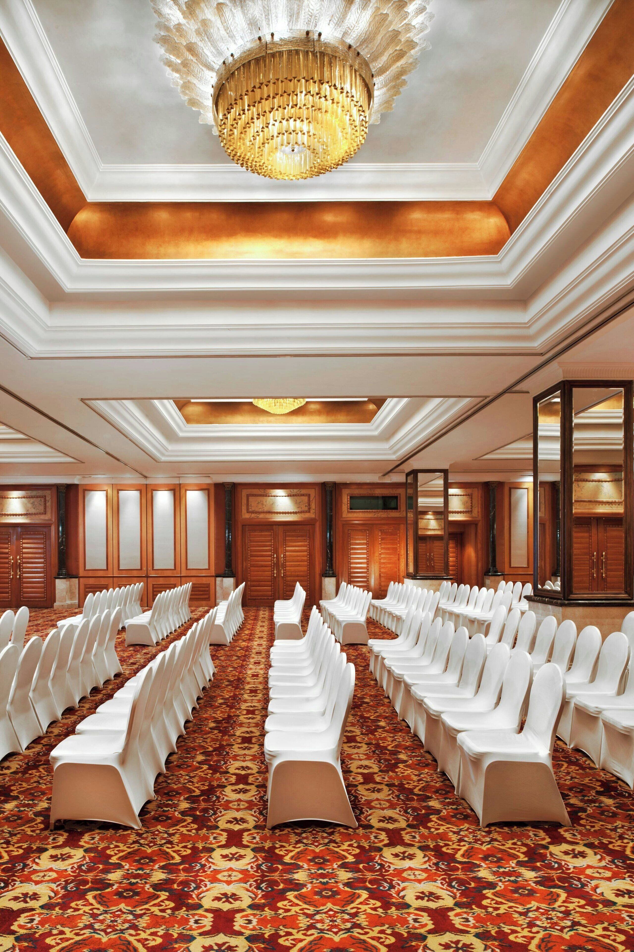 A conference room with rows of white chairs, a patterned carpet, and a large chandelier.