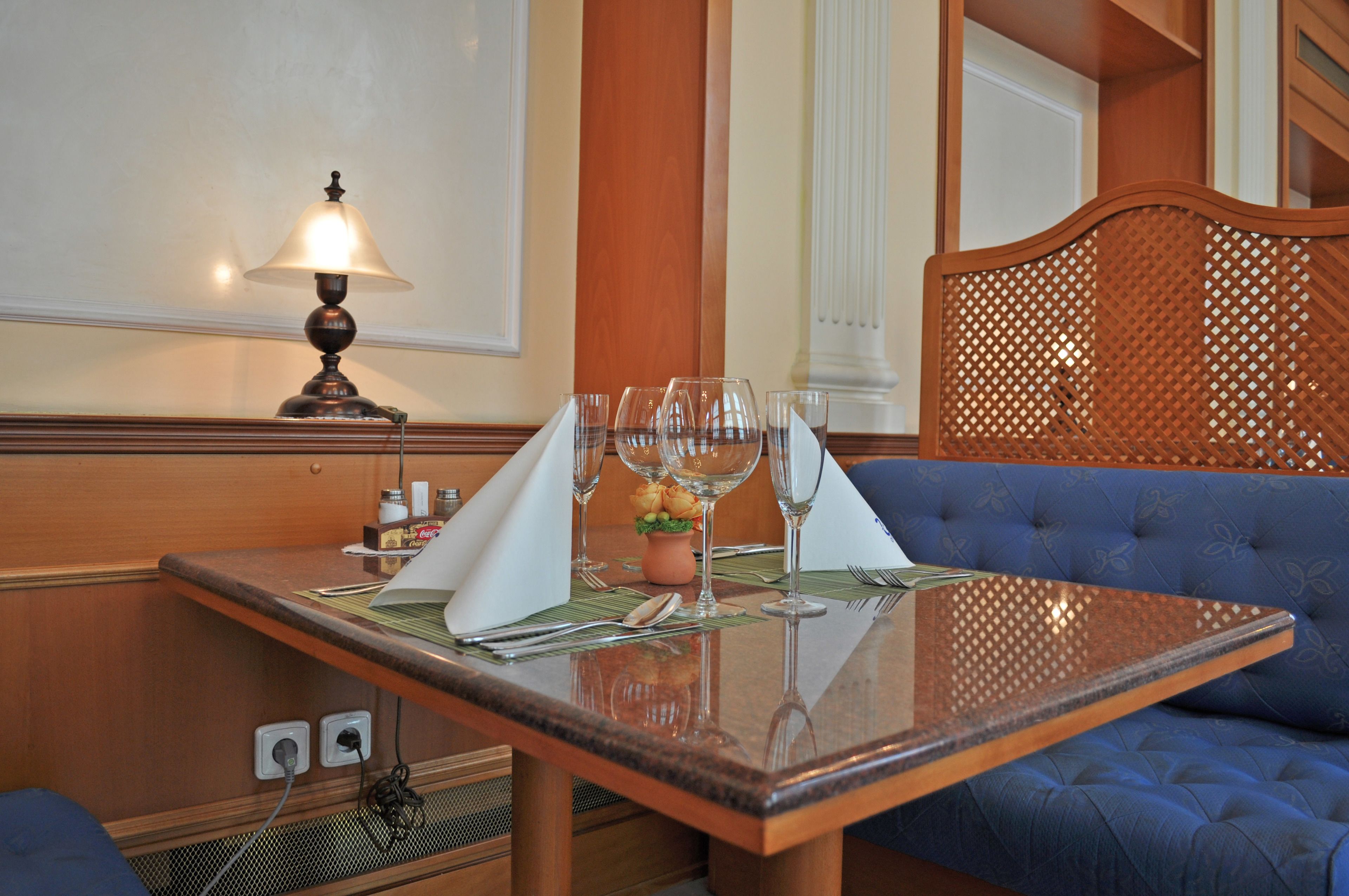 Un comedor con una mesa preparada para dos personas, una lámpara y un banco tapizado en azul.